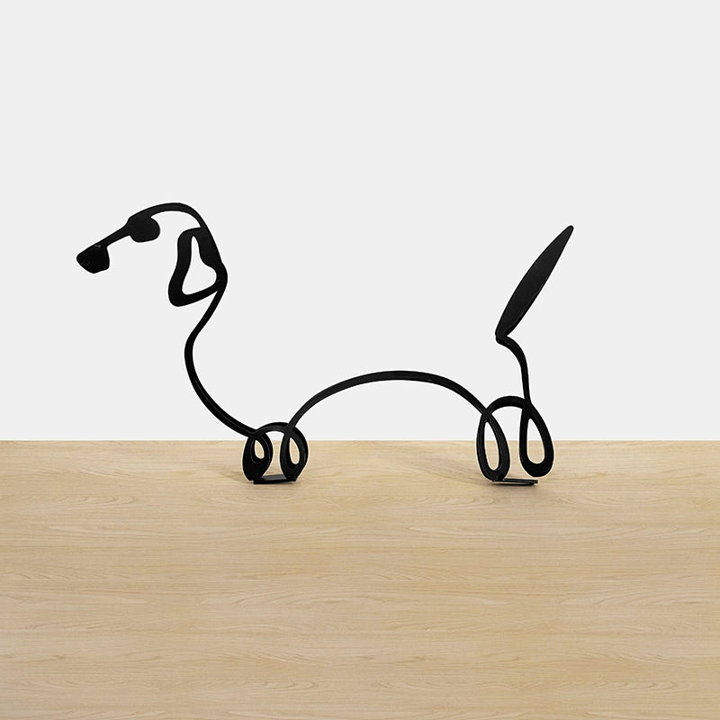 Black wire dog sculpture on a wooden surface with a white background