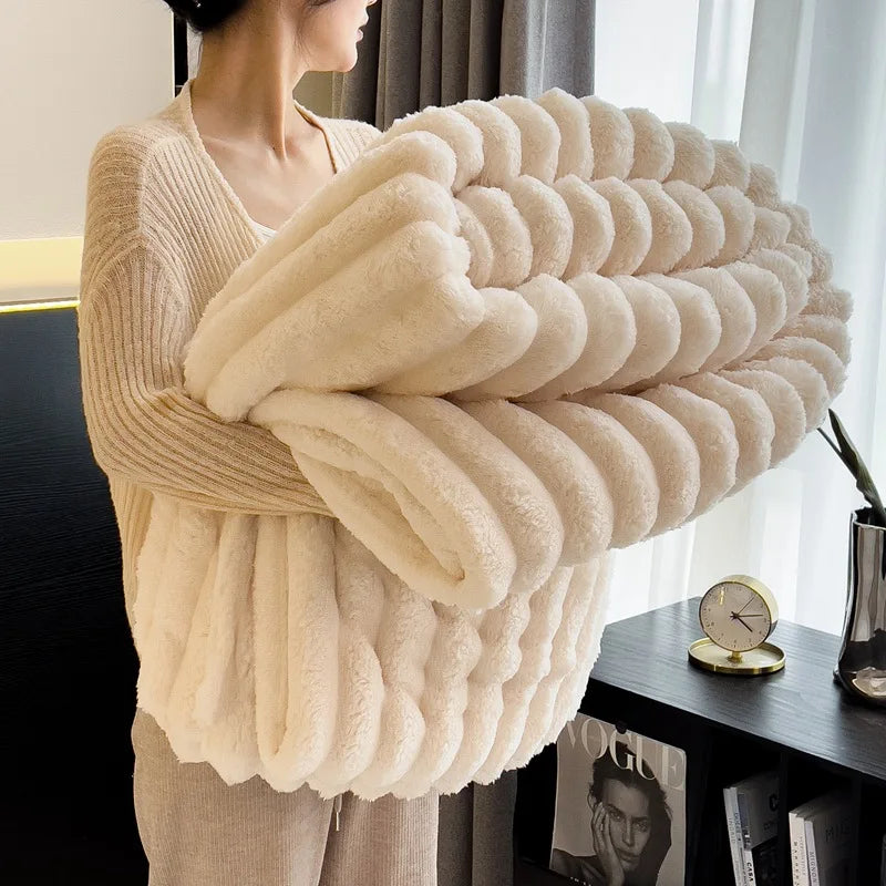 Person holding a large cream-colored knitted blanket in a room with a window and decor.