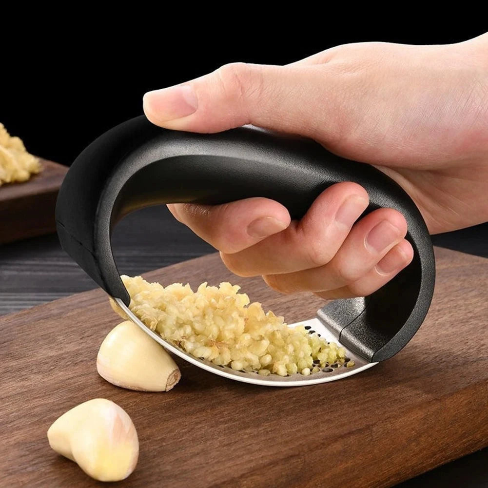 Hand using a garlic press on a wooden cutting board with garlic cloves.