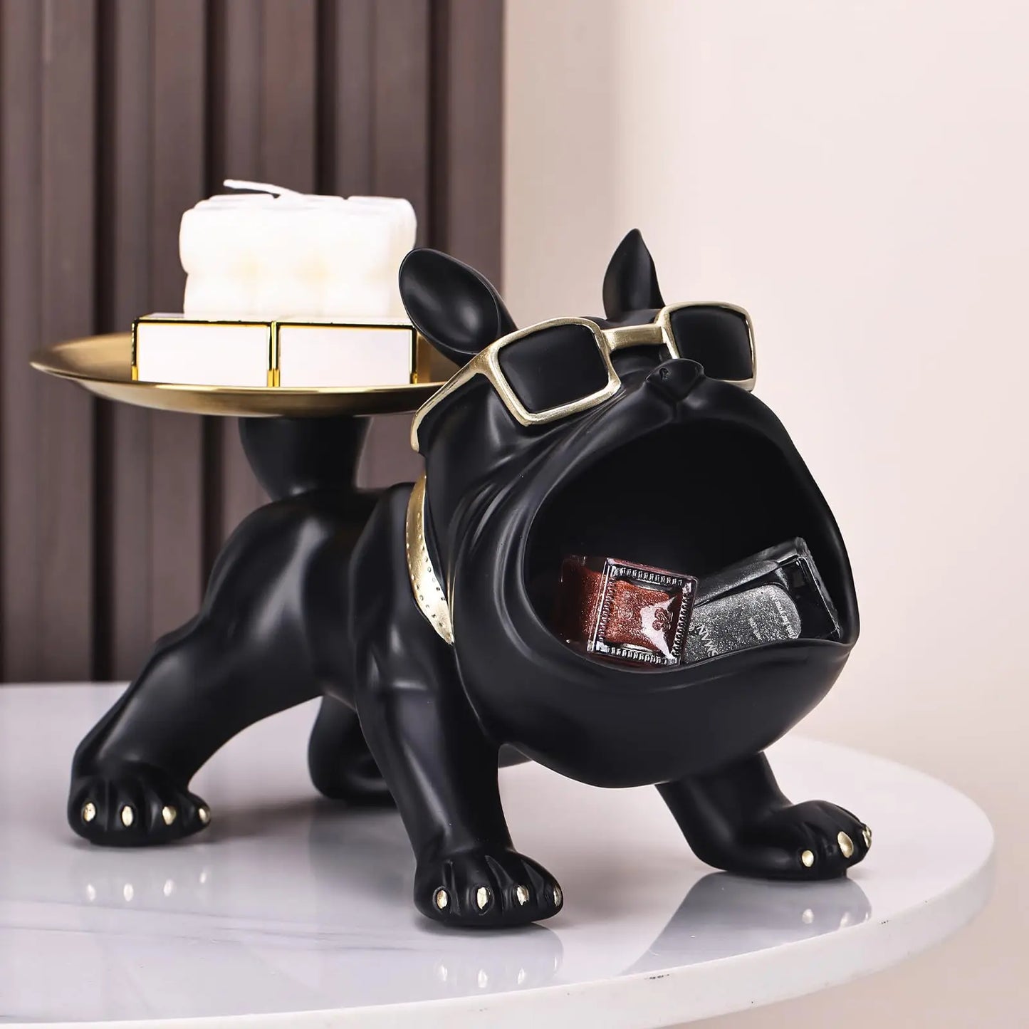 Black dog-shaped figurine with sunglasses holding a box on a white surface.