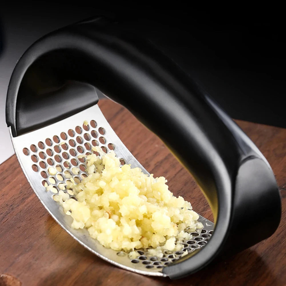 Black garlic press with minced garlic on a wooden surface