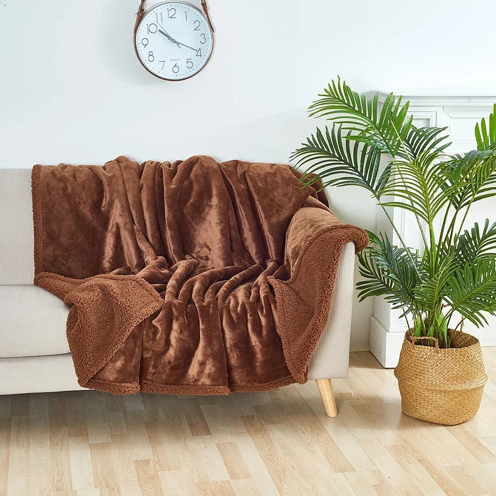 Brown blanket draped over a white sofa with a clock on the wall and a plant in the corner.