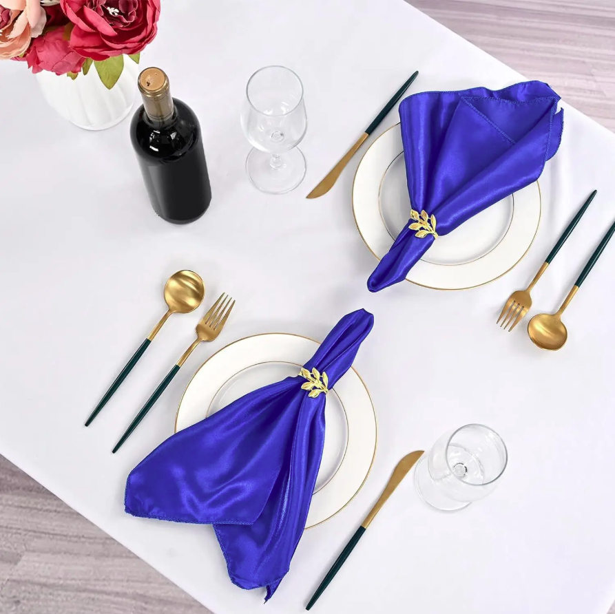 Dining table setting with blue napkins, gold cutlery, and a bottle of wine.