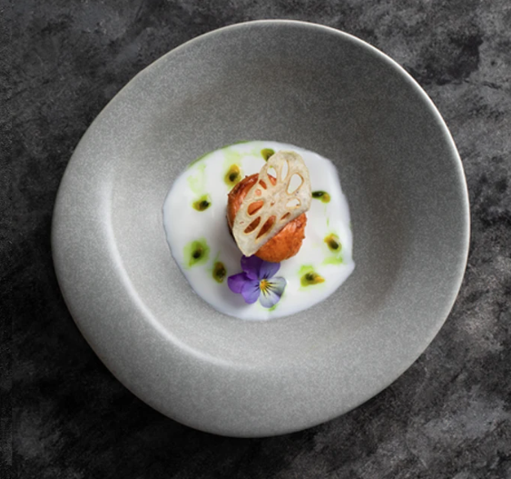 Delicate dish with seafood and vegetables on a gray plate against a dark background