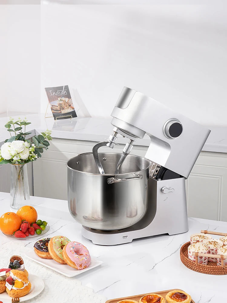 Stainless steel stand mixer on a kitchen counter with baked goods and fruits.