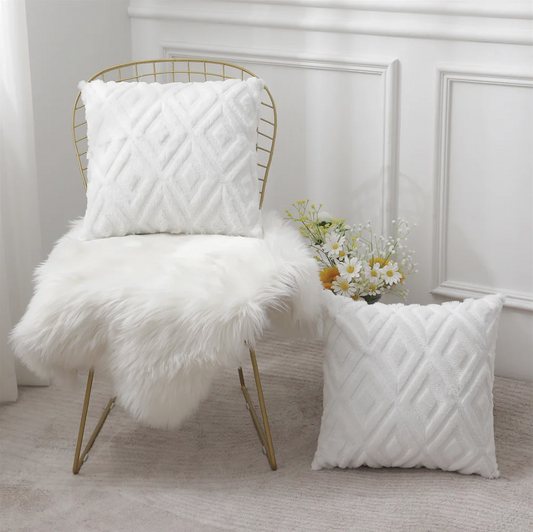 White textured pillow on a gold chair with a white fur throw and flowers in the background.