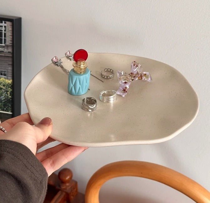 Person holding a round beige tray with decorative items including a blue bottle and pink flowers.