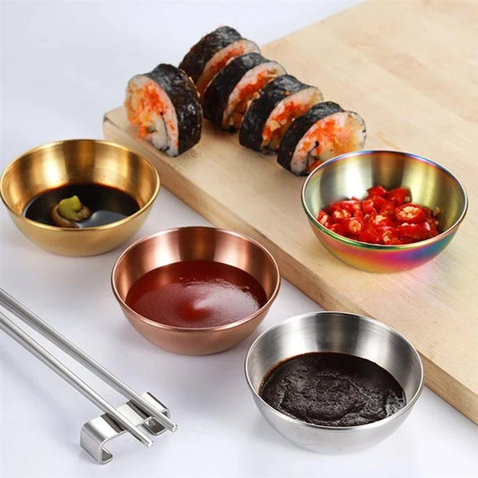 Sushi with various sauces in metallic bowls on a wooden board.