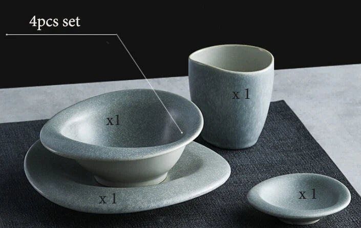 Set of four ceramic items including a bowl, cup, and two smaller dishes on a dark surface with a light gray background.