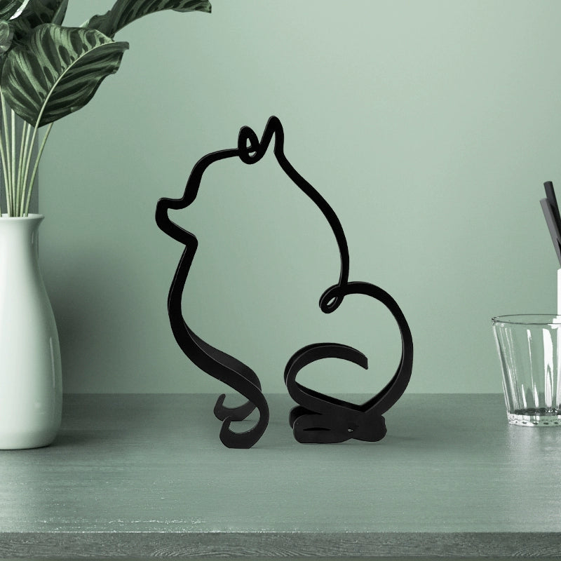 Black wire sculpture of a cat on a green surface with a plant and glass in the background