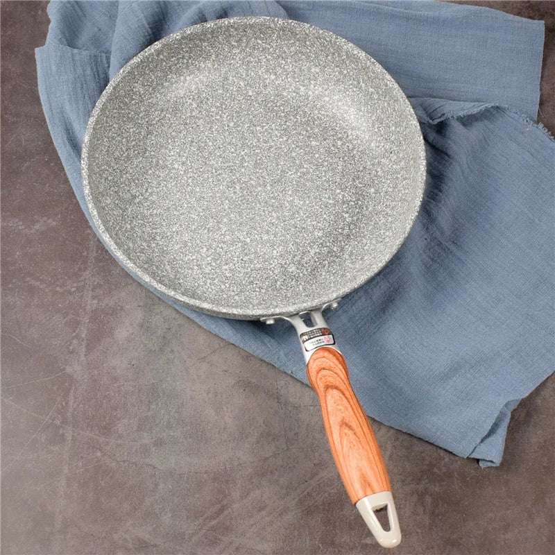 Frying pan with a speckled non-stick surface and wooden handle on a blue cloth.