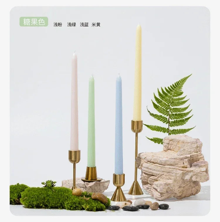 Decorative setup with candles in gold holders, a fern, and stones on a white background.
