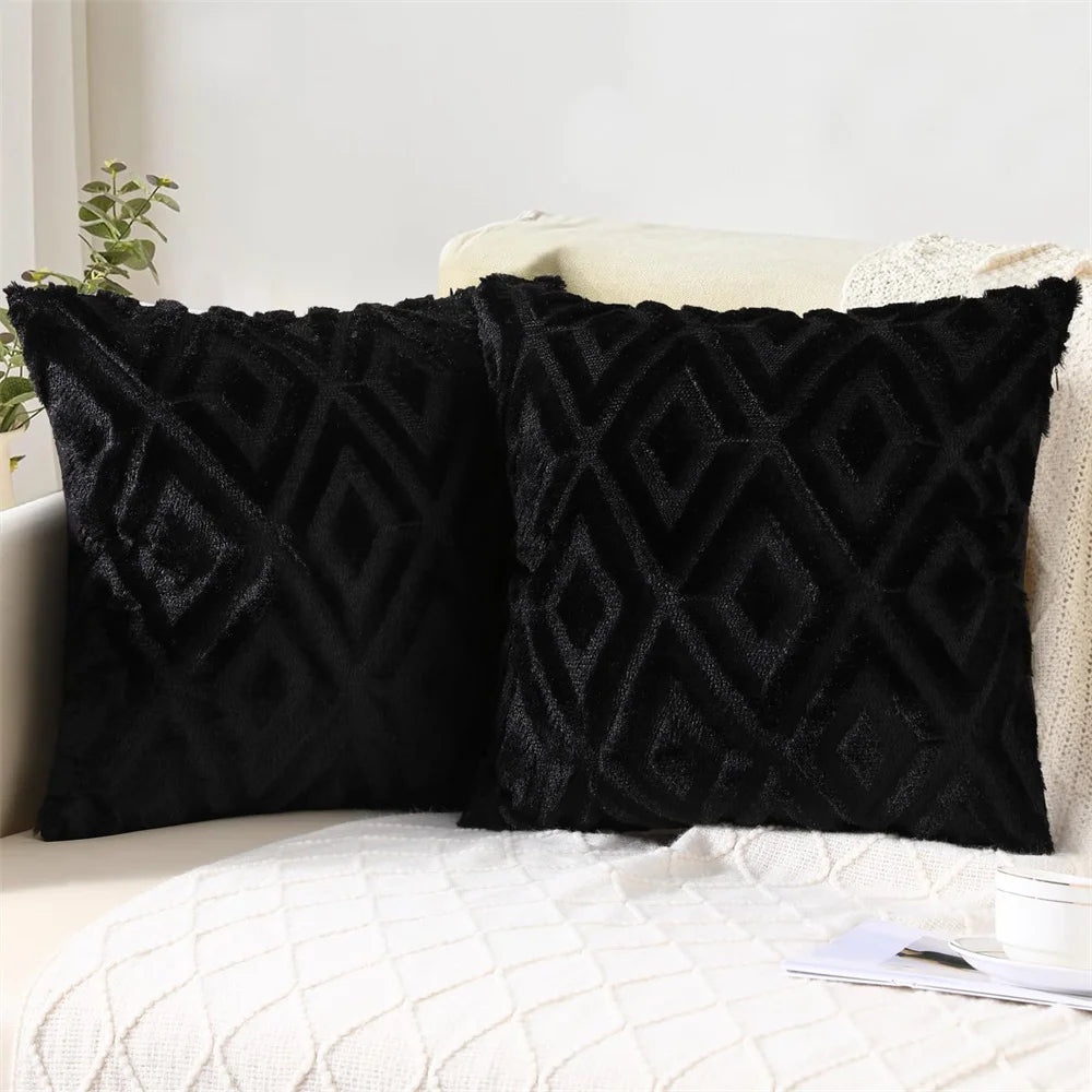 Two black textured pillows on a white couch with a plant in the background.