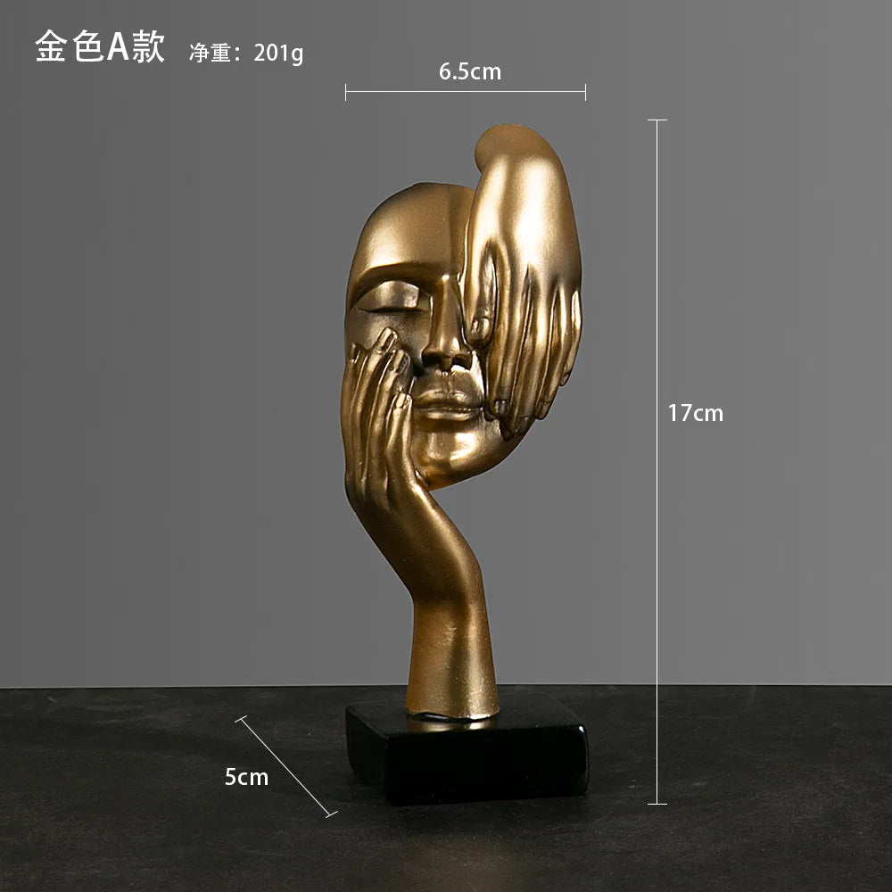 Gold abstract sculpture of a face and hand on a dark surface with: 5cm x 17cm x 6.5cm