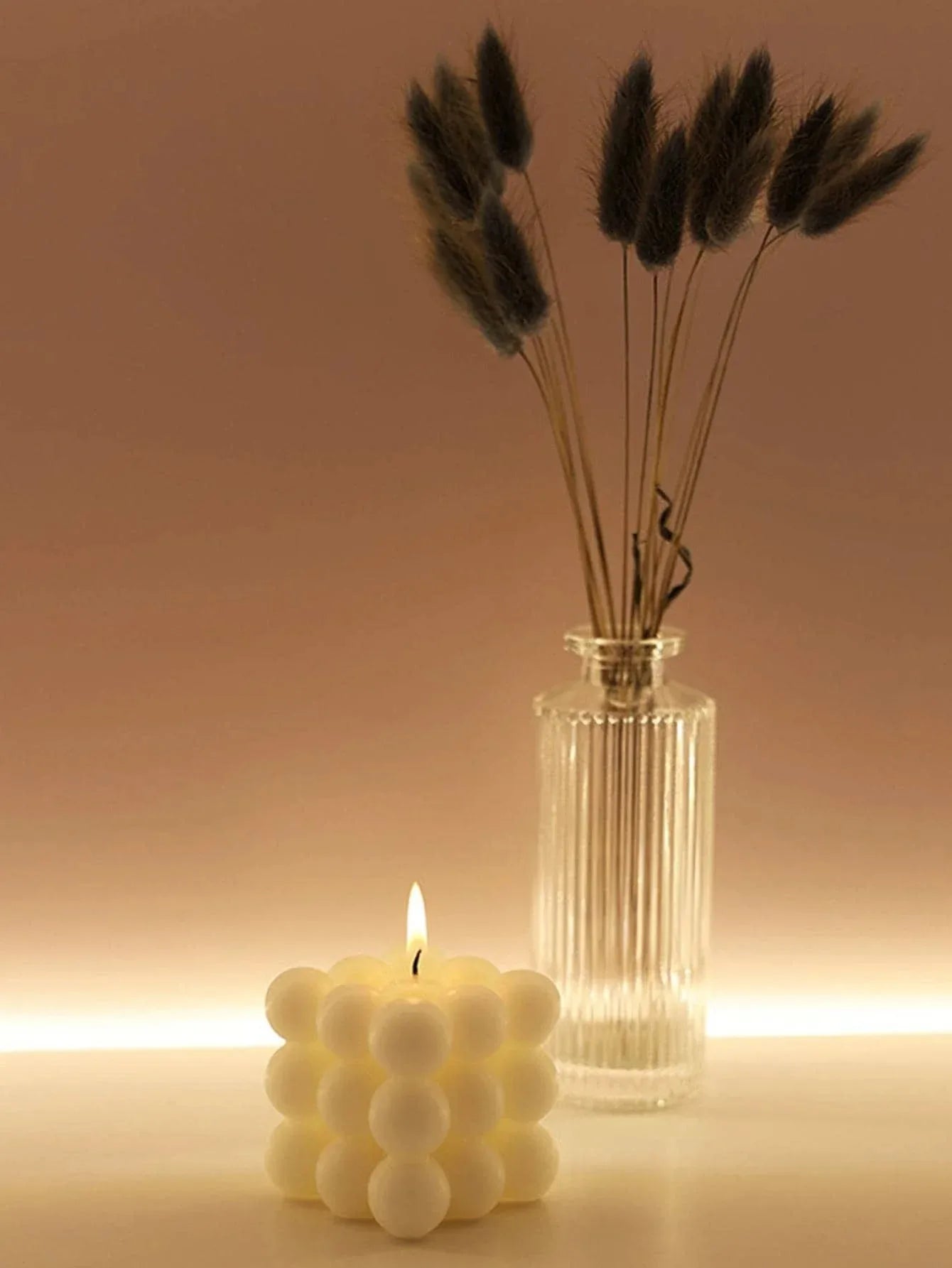Candle with a bubble design and a vase with dried grasses on a warm-toned background