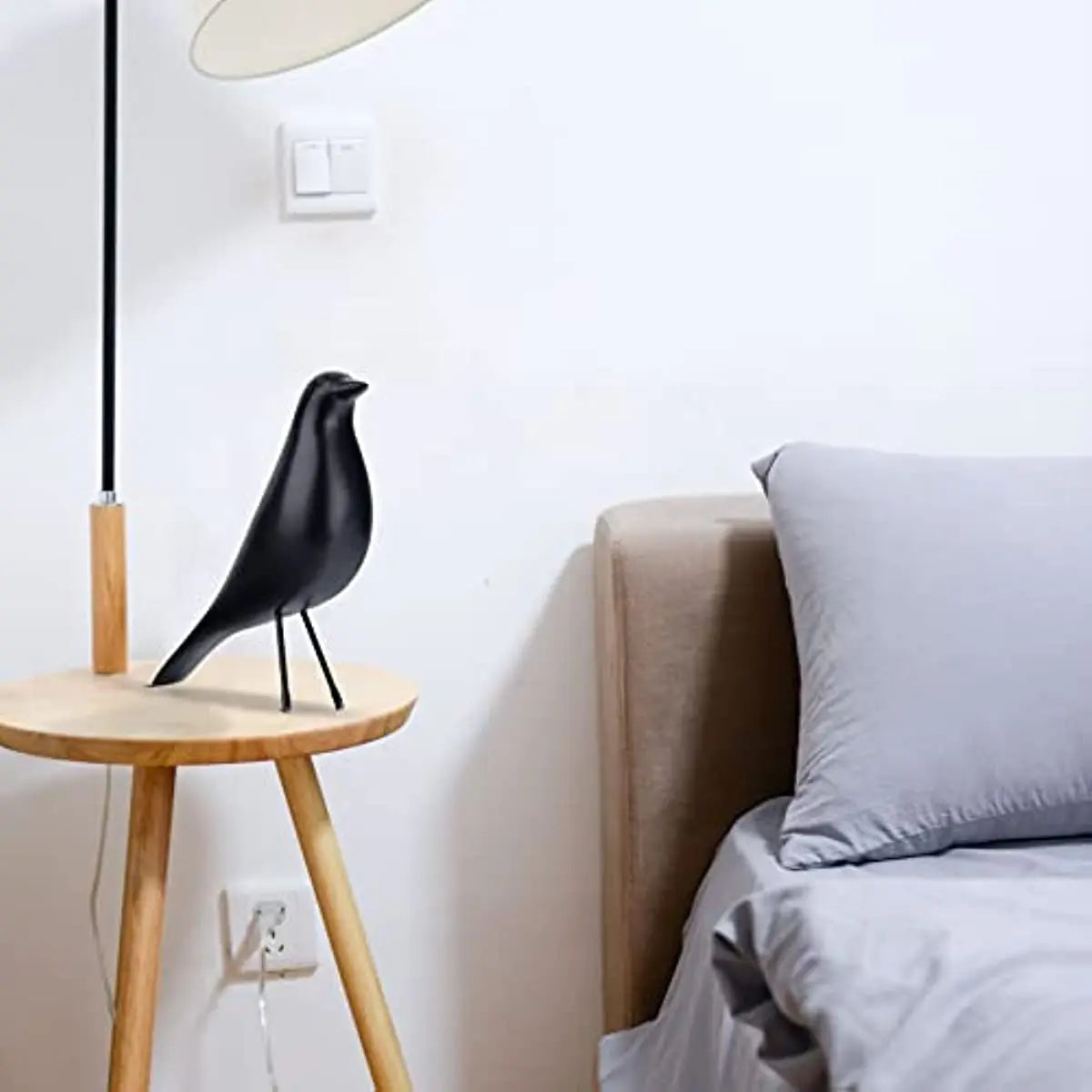 Black bird sculpture on a wooden side table next to a bed with gray bedding.