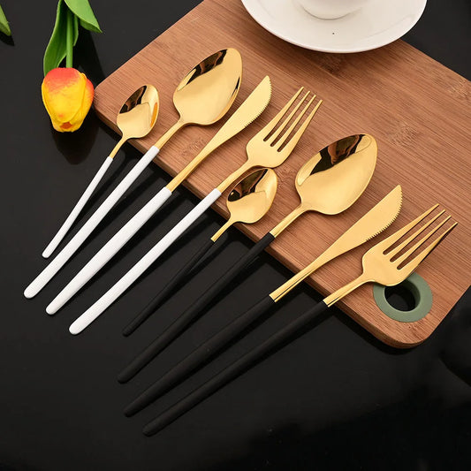 Set of gold, white, and black cutlery on a wooden board with a tulip flower.