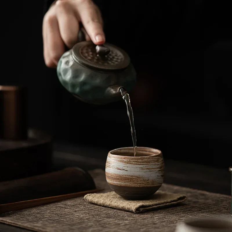 Tea being poured from a ceramic teapot into a cup on a dark background