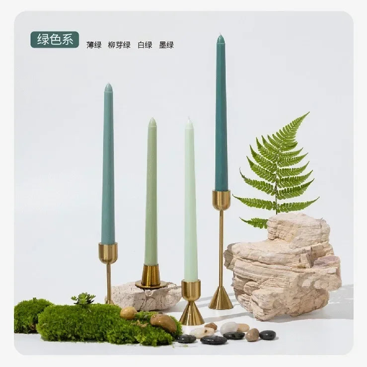 Decorative setup with green candles in gold holders, rocks, and ferns on a white background