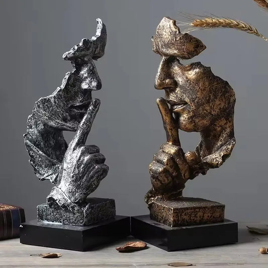 Two sculptures of man faces posing a "Shush" at each other on a gray background