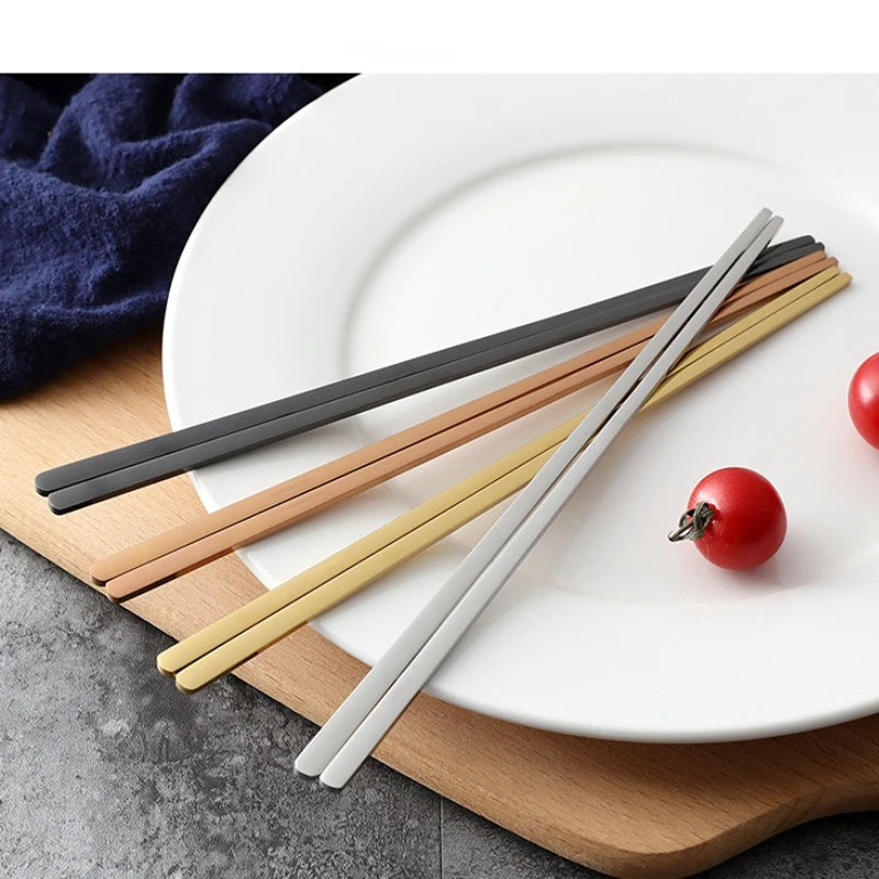 Set of four chopsticks in different colors on a white plate with a wooden board and tomatoes.