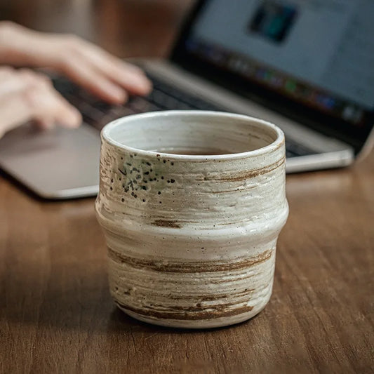 Ceramic cup on a wooden table with a blurred laptop in the background