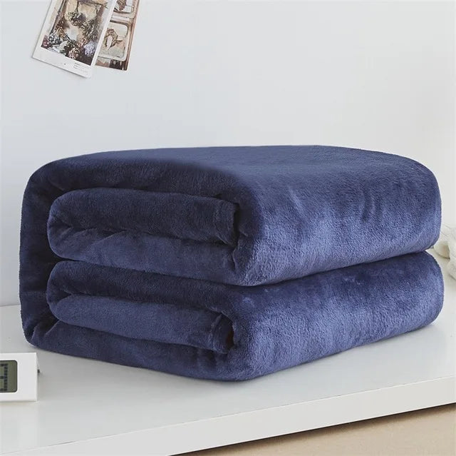Folded navy blue blanket on a white surface with a light gray wall in the background.