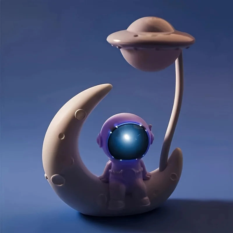 Toy figure of a small alien on a moon with a UFO above, against a blue background