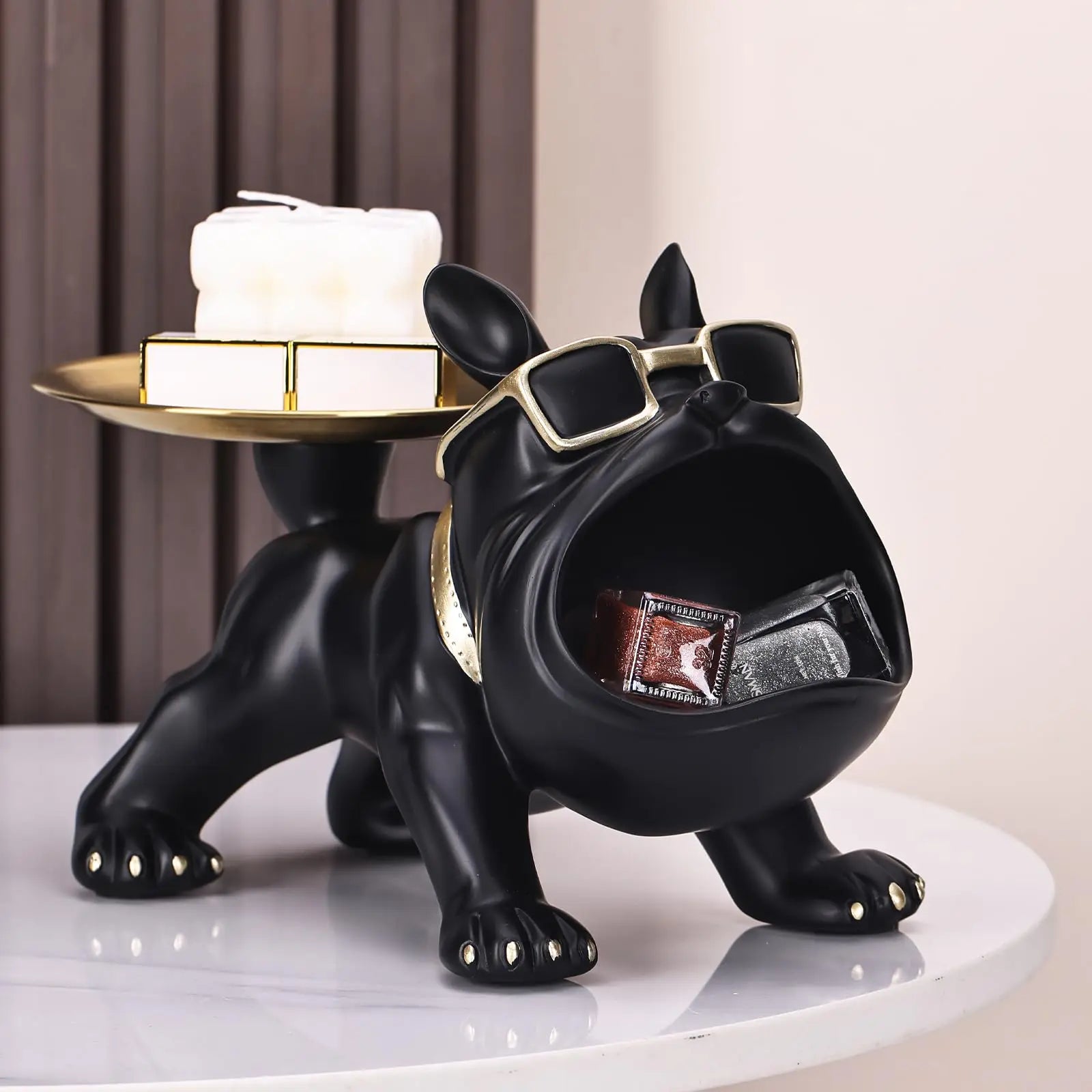 Black dog-shaped figurine with sunglasses holding a box on a white surface.