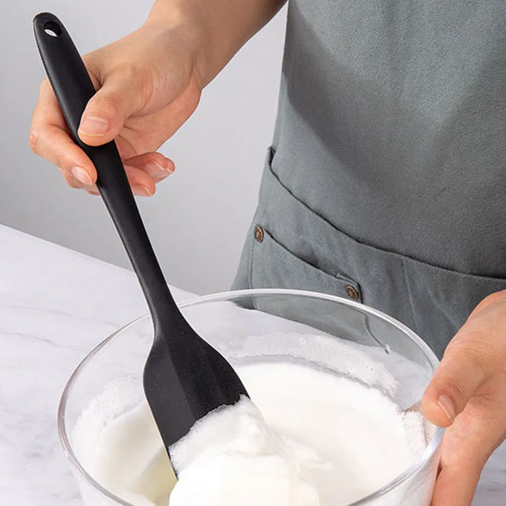 Person using a black spatula to mix white cream in a glass bowl.