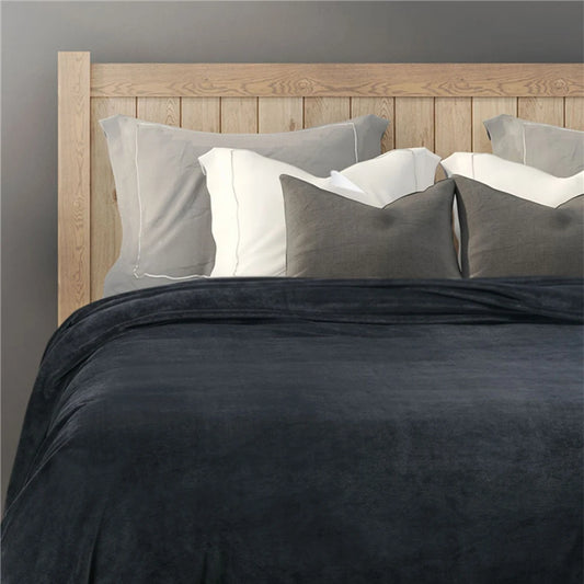 Bed with dark gray comforter and pillows against a wooden headboard.
