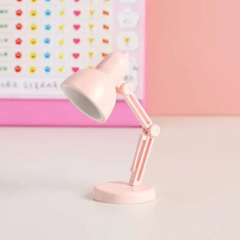 Pink desk lamp on a light surface with a colorful heart-patterned board in the background.