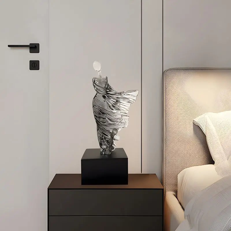 Decorative resin sculpture on a nightstand next to a bed with white bedding.