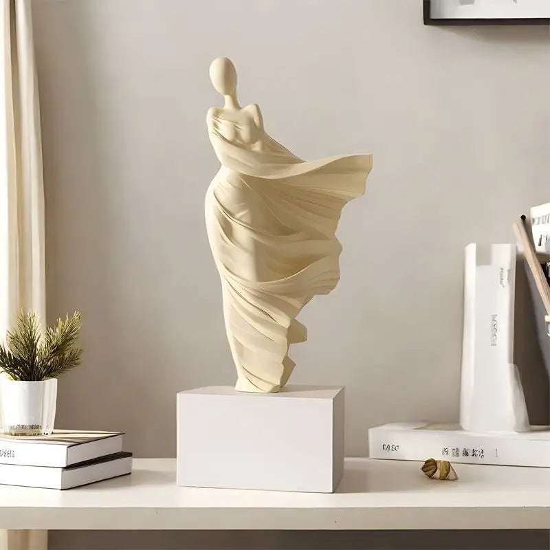 Decorative sculpture of a draped figure on a white surface with books and a plant.