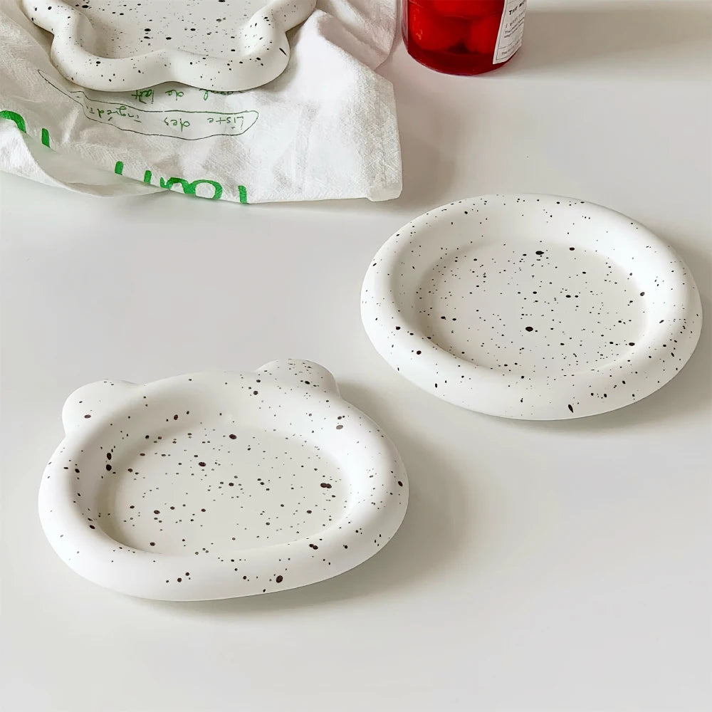 Two speckled ceramic coasters on a white surface with a red cup and green text towel in the background.
