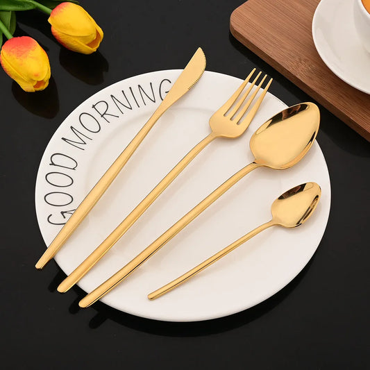 Gold cutlery set on a white plate with 'GOOD MORNING' text, surrounded by yellow tulips on a black surface.