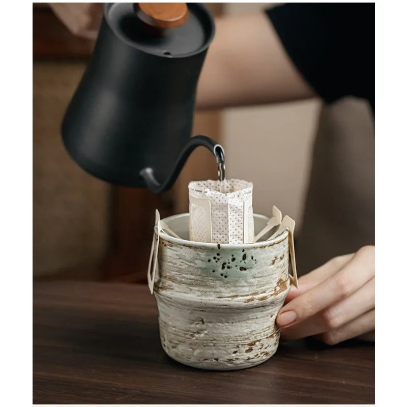 Person pouring tea from a black teapot into a ceramic filter basket.