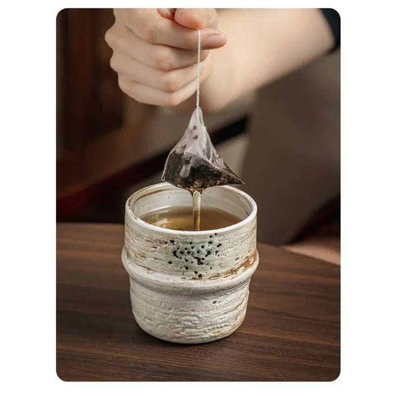 Tea bag being dripped into a ceramic cup on a wooden surface