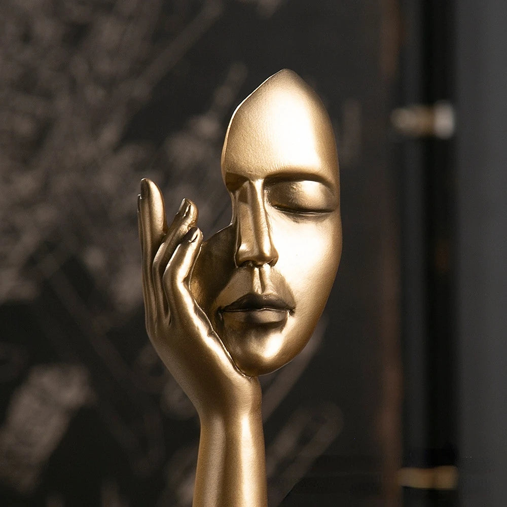 Gold statue of a hand holding a face against a dark background