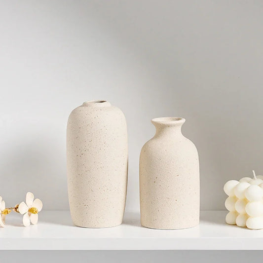 Two beige ceramic vases on a light gray surface with a plain background