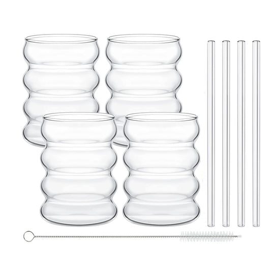 Set of clear glass tumblers with wave-like design and four straws on a white background