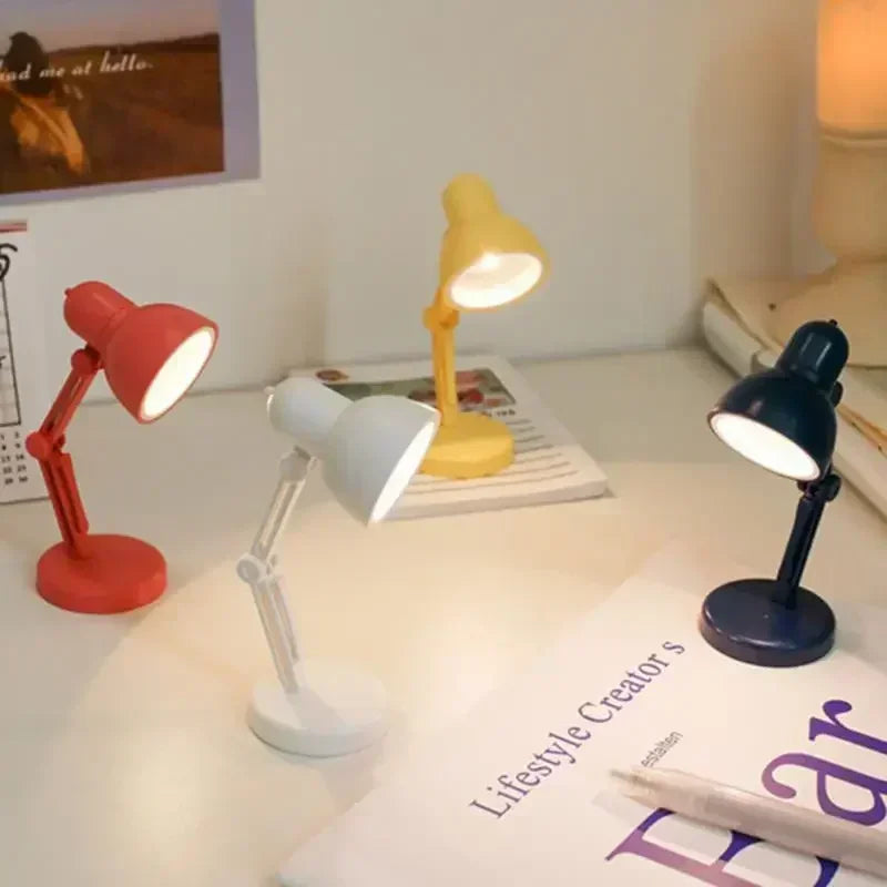 Four colorful desk lamps on a surface with books and a pen.