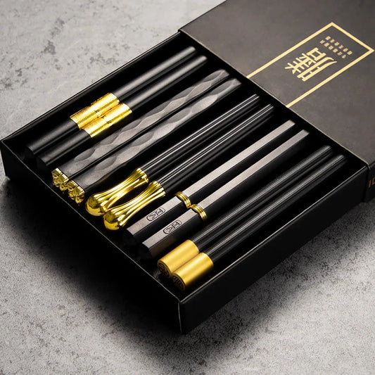 Set of black and gold chopsticks in a black box on a gray surface