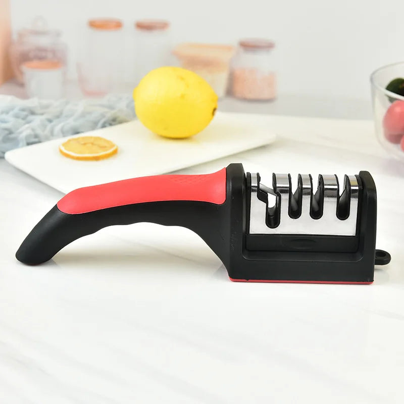 Knife sharpener with red handle on a white surface, lemon and cutting board in the background