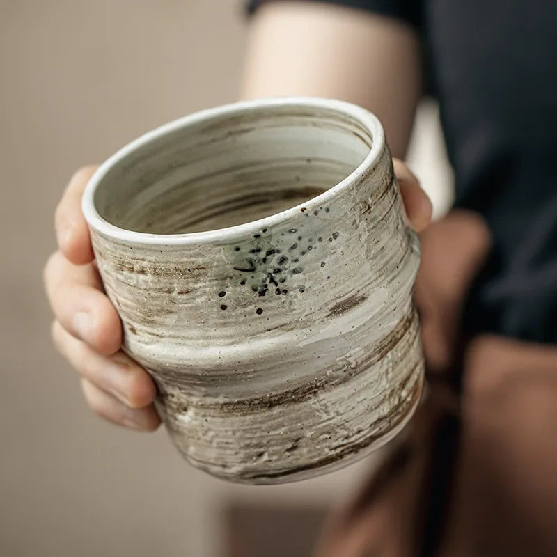 Person holding a textured ceramic cup against a neutral background