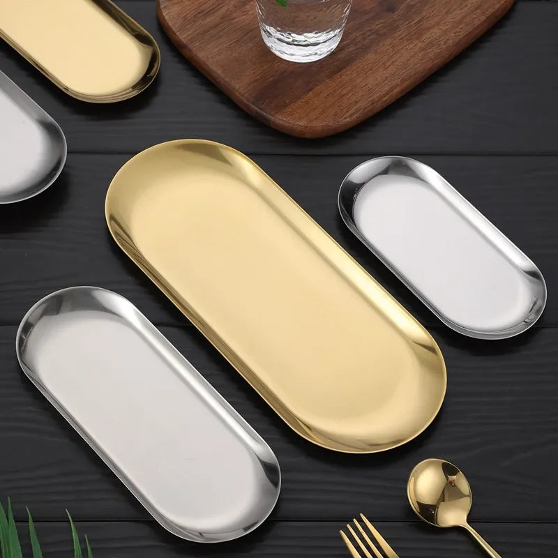 Gold and silver oval trays on a dark surface with a wooden board and glass.