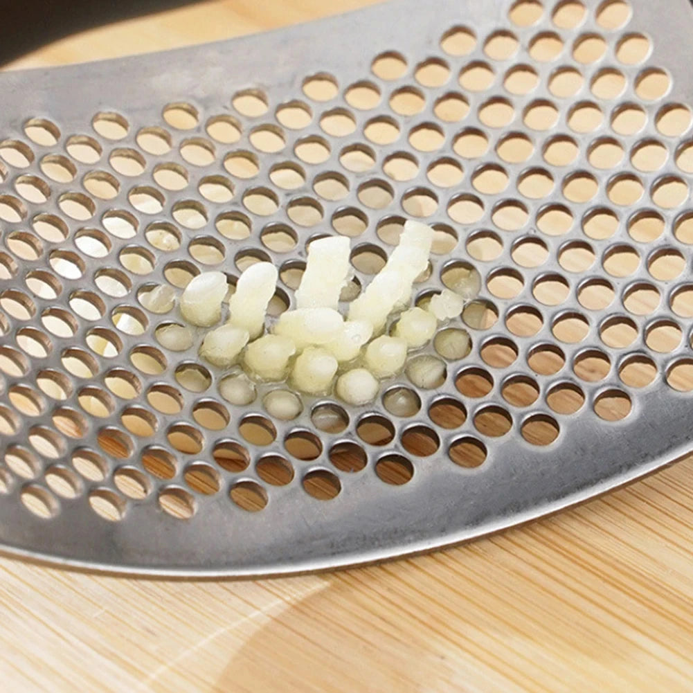 Metallic grater with a small pile of chopped garlic on a wooden surface