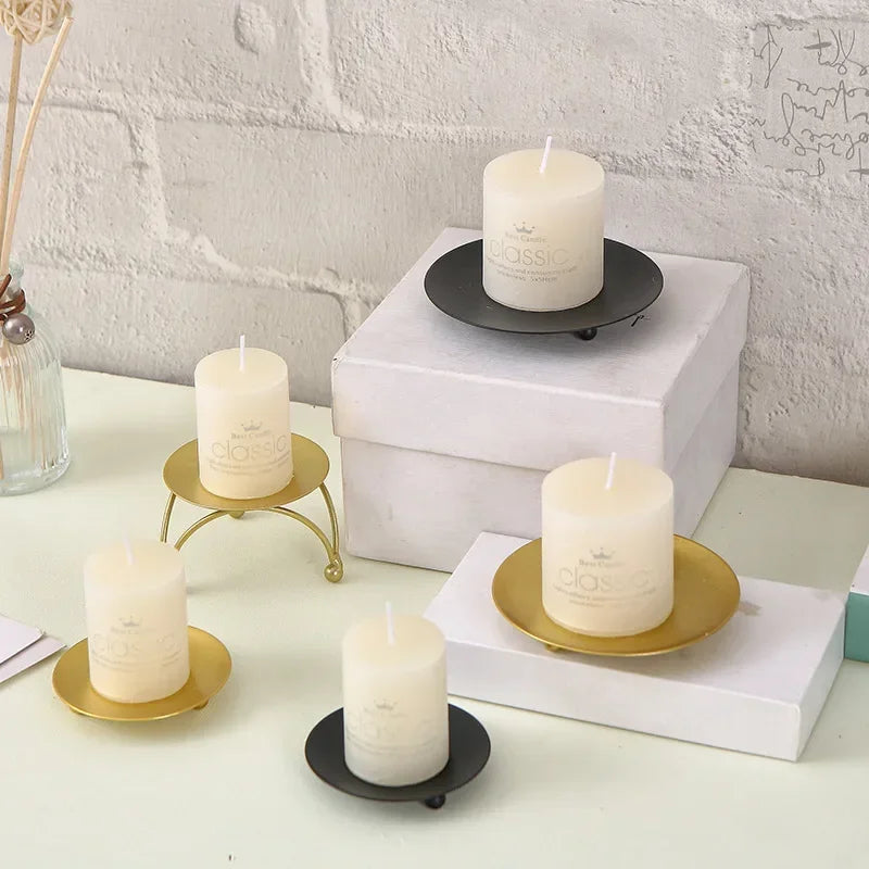 White candles on gold and black holders against a light gray brick wall.