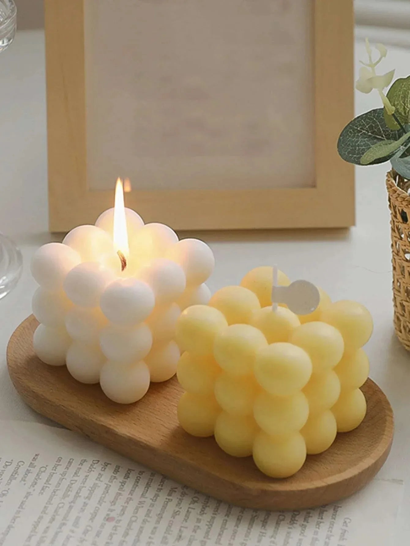 Two bubble-shaped candles on a wooden tray with a light background