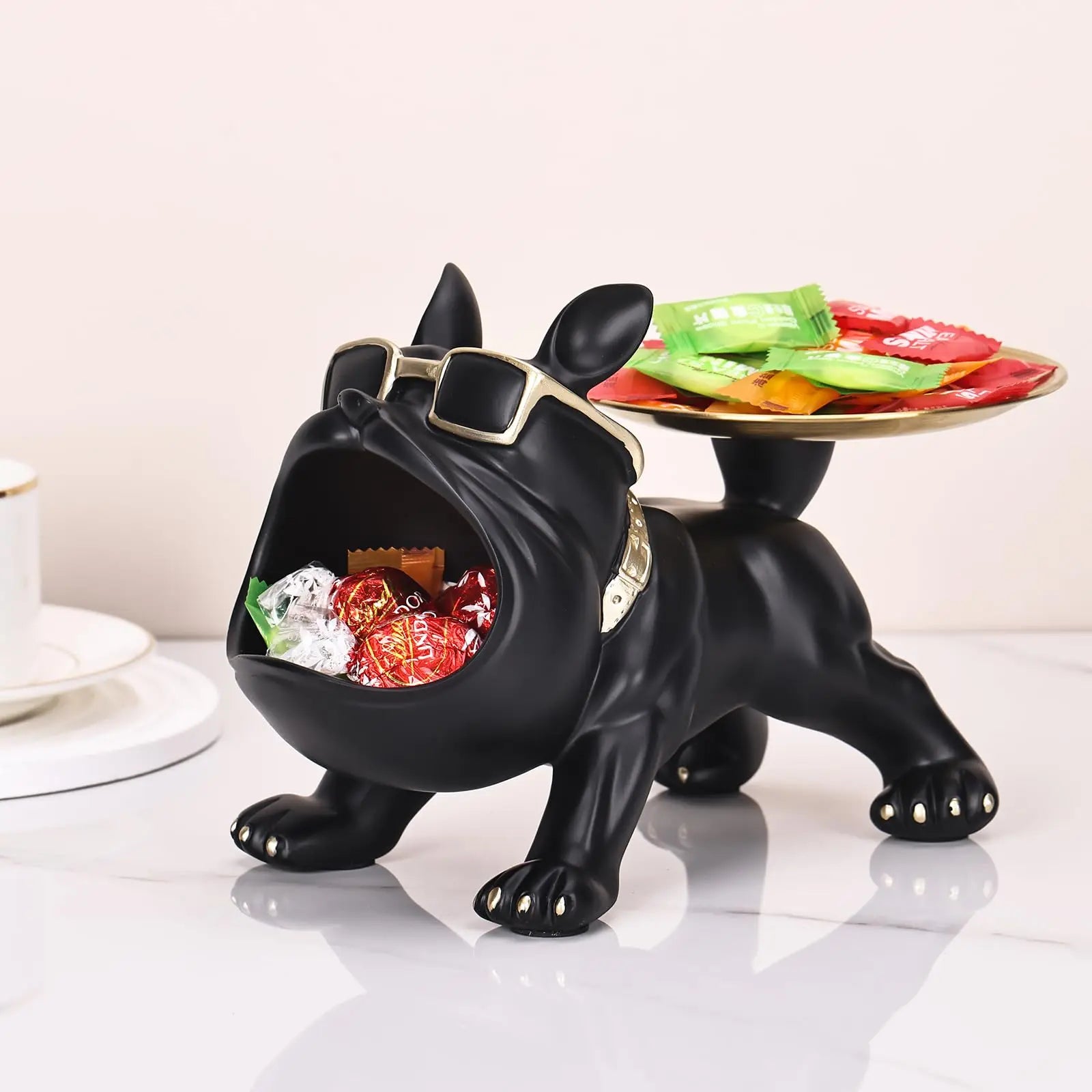 Black dog-shaped candy dish with a tray of snacks on a white surface.